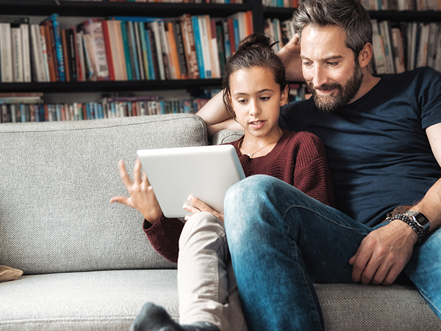 Father and daughter sitting on sofa looking at digital tablet 