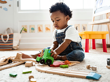 Child playing on the floor looking at a wood train